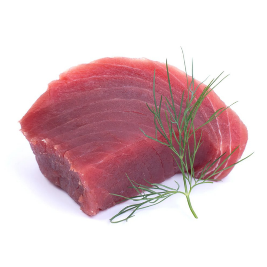 Raw tuna steak with deep red flesh and visible grain, garnished with fresh dill on a white background